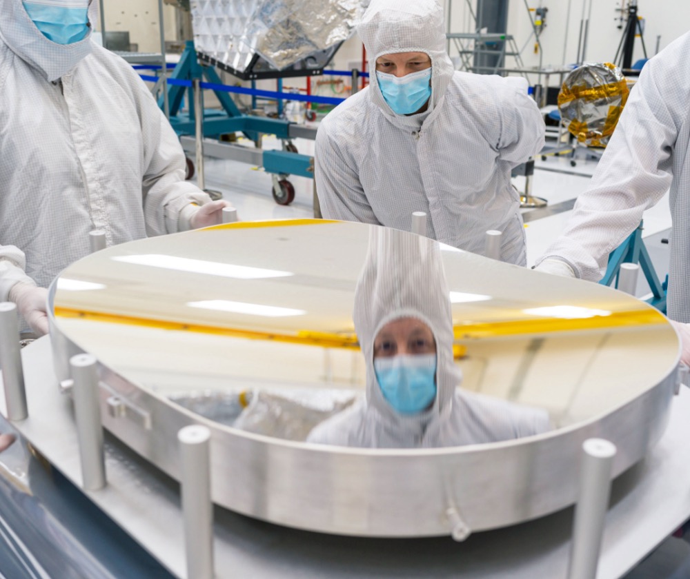 A mirror that was later installed inside the telescope for NASA’s Near-Earth Object Surveyor shows a reflection of principal optical engineer Brian Monacelli during an inspection of the mirror’s surface at the agency’s Jet Propulsion Laboratory