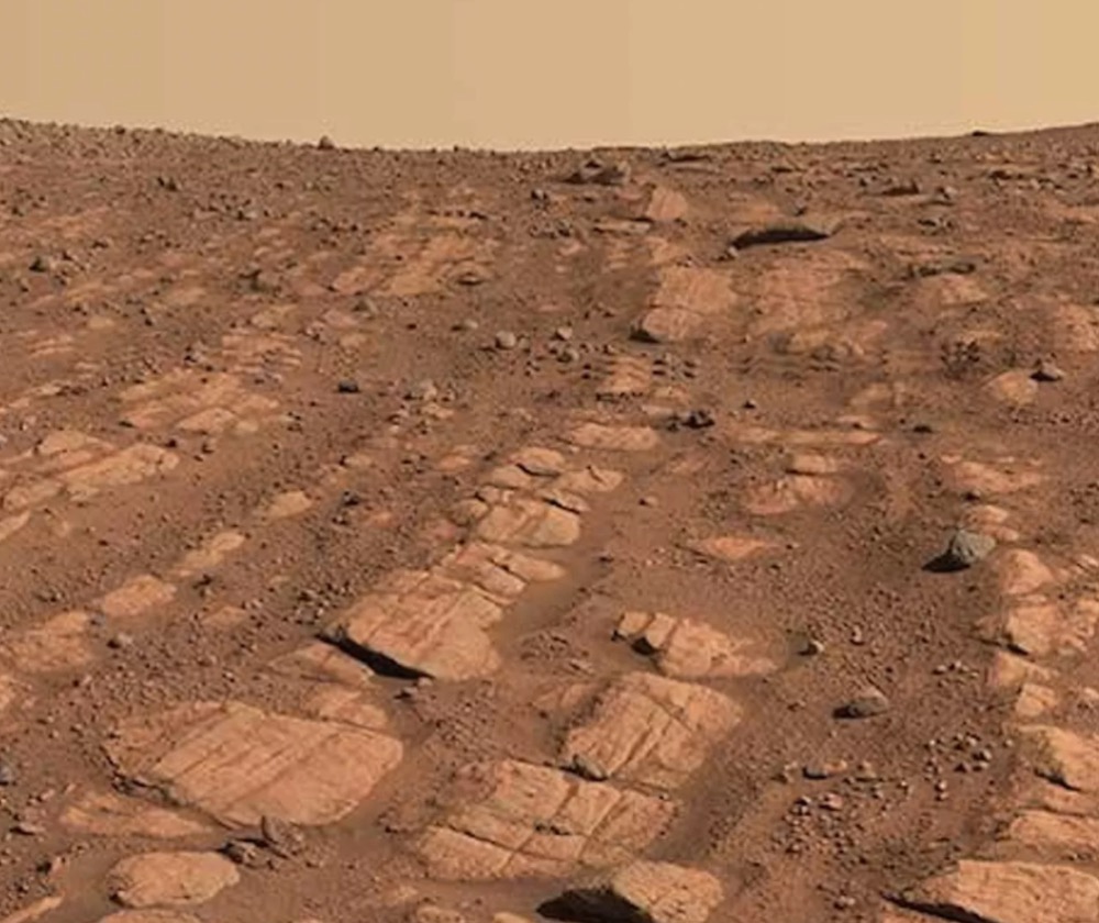 View of mars captured by the perseverance rover showing bands of light-colored rock in the reddish dirt, presumably indicated ancient water channels
