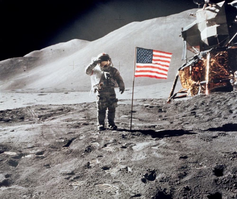 Astronaut David R. Scott, commander, gives a military salute while standing beside the deployed United States flag during the Apollo 15 lunar surface extravehicular activity (EVA) at the Hadley-Apennine landing site